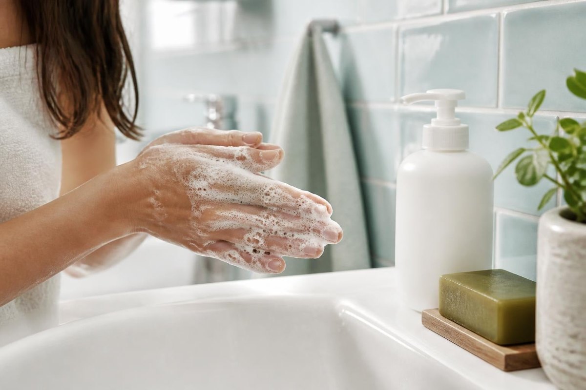 Hands lathering a sulphate-free shampoo at a bathroom basin, with an unbranded pump bottle and a bar of castile soap