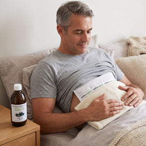 Man relaxing in bed wearing a castor oil liver compress wrap with organic castor oil on the bedside table